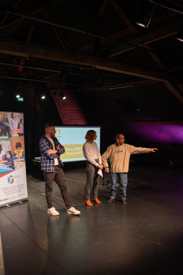 Une personne accompagnée interiewée montre quelque chose du doigt. À côté d'elle, un professionnel du Gapas et l'animatrice de la soirée.